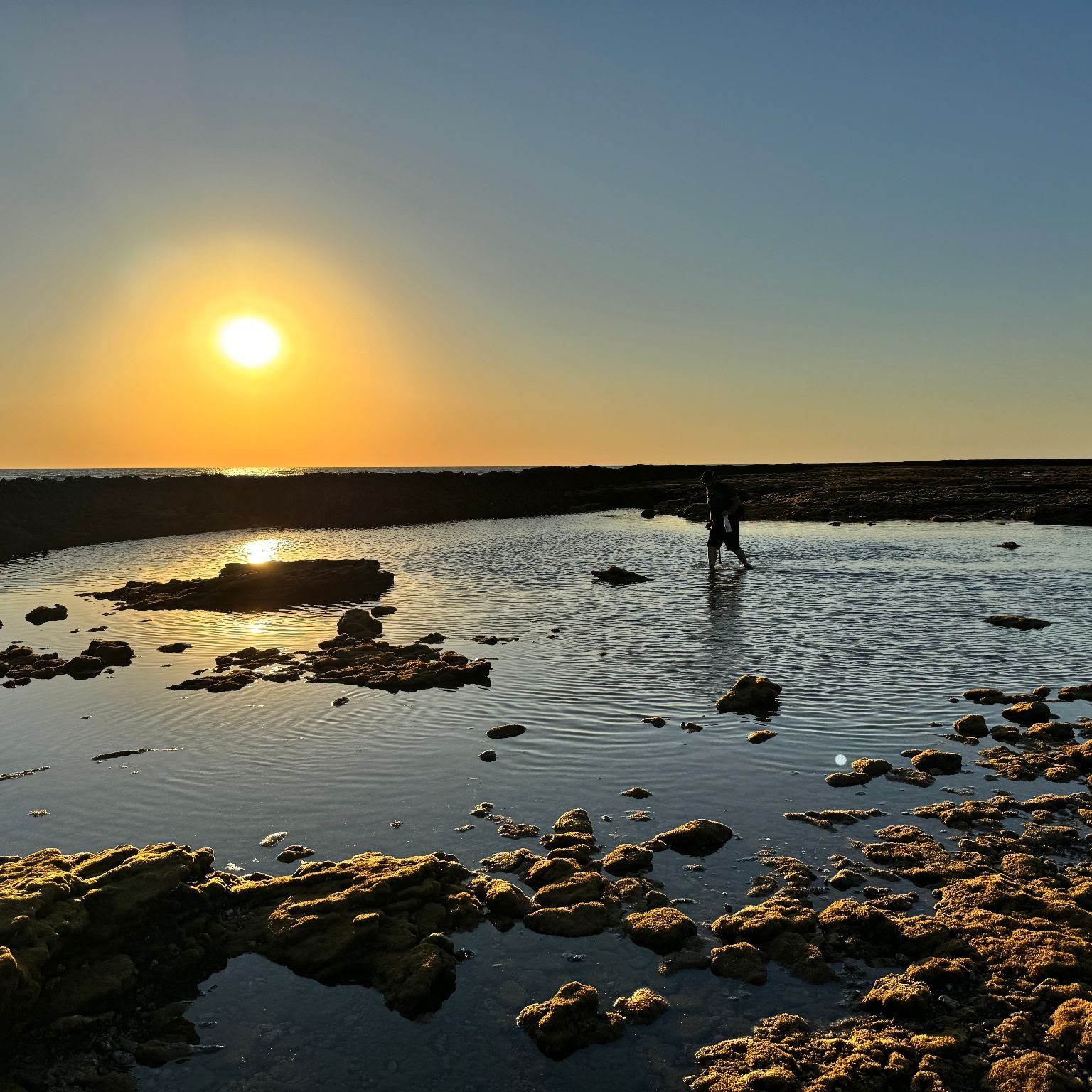 Un corralero camina con la atarraya por una poza de los corrales al atardecer