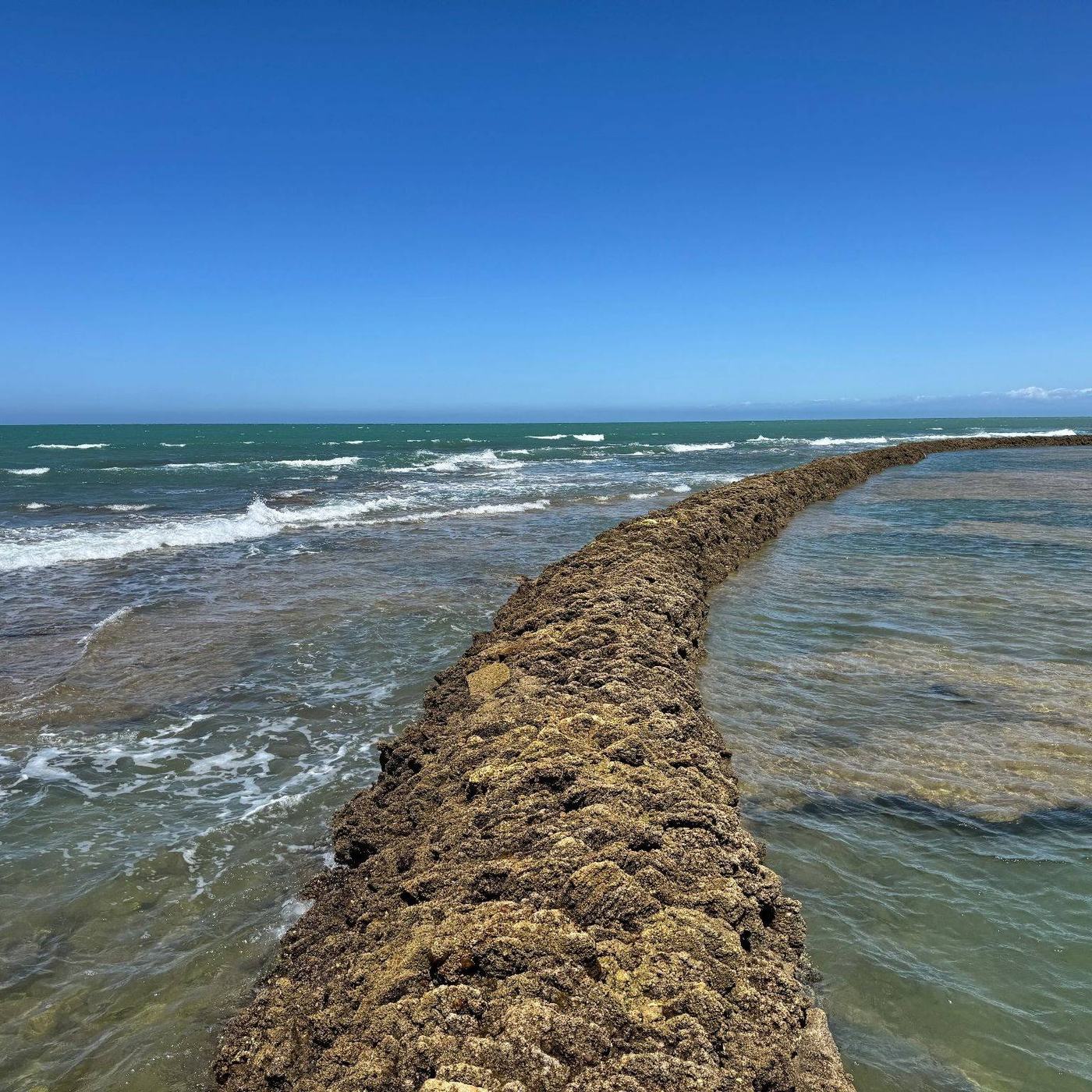 Muro de piedra de un corral adentrándose en el mar con el agua turquesa a ambos lados